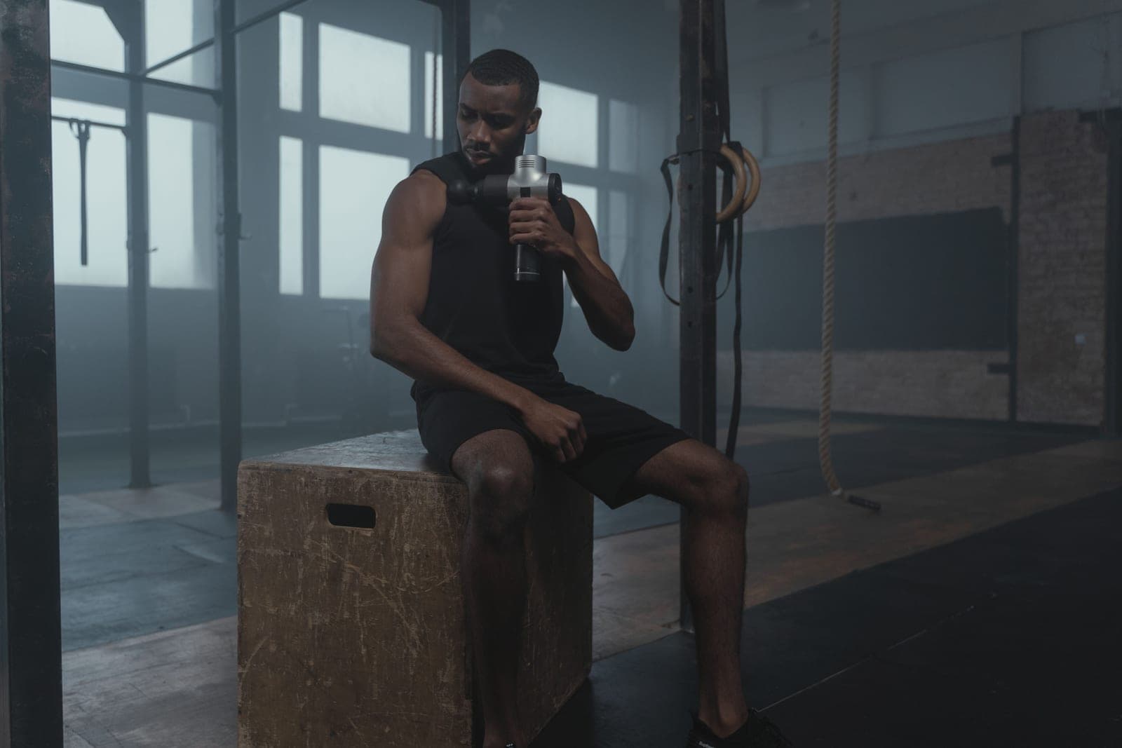 An athlete using a percussion massage gun on a leg after training